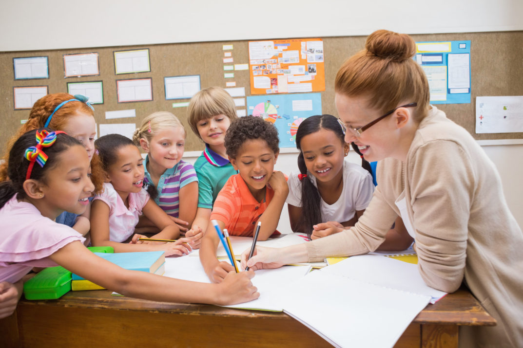 teacher and pupils working at desk together at the elementary school