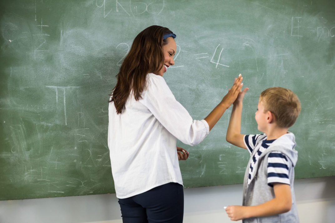 happy teacher and school boy giving high five in classroom at school