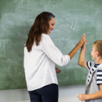 happy teacher and school boy giving high five in classroom at school