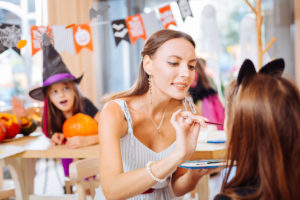 Kindergarten teacher holding paintbrush while painting faces for Halloween