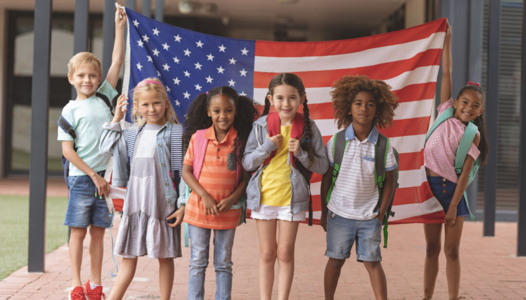 Group of young students standing in front of a large American flag; teaching citizenship concept