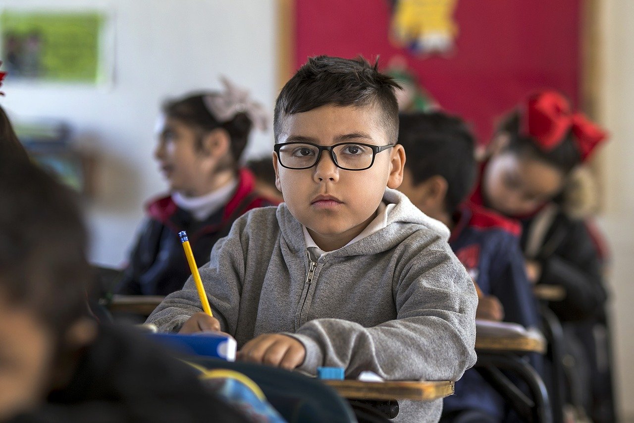young student with glasses stares at camera; fall 2021 return to classroom concept