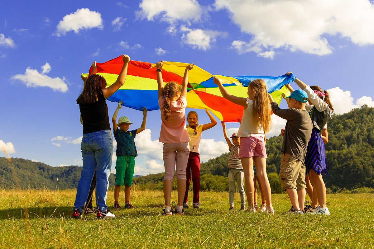 children outdoors playing with a colorful parachute; returning students concept