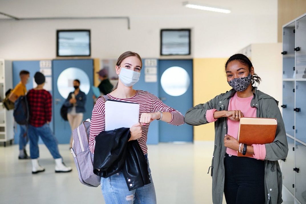 Young students friends with face masks back at college or university greeting, coronavirus concept.