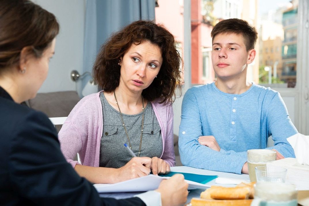 Positive woman with teenager boy discussing documents with financial adviser
