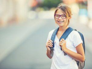 Schoolgirl with bag, backpack. Portrait of modern happy teen school girl with bag backpack. Girl with dental braces and glasses.