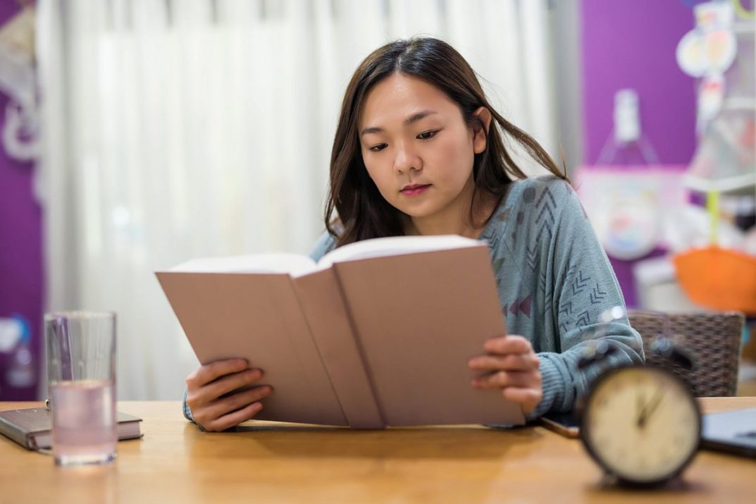 Academic female Student in house read big text book on working table with copy space for text. Serious Asian girl prepare for final exam. Graduated education concept.