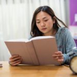 Academic female Student in house read big text book on working table with copy space for text. Serious Asian girl prepare for final exam. Graduated education concept.