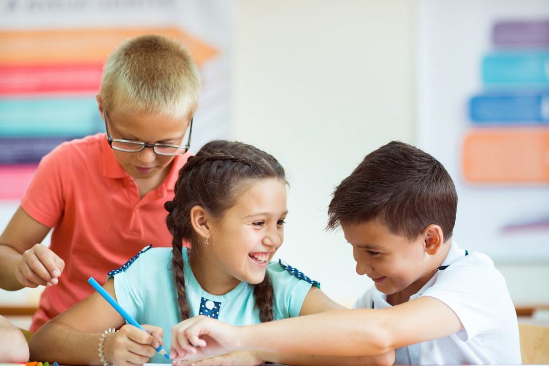 Happy elementary students sitting at desk and joyful discussing in classroom at school