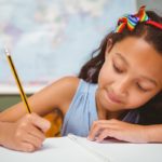 Portrait of cute little girl writing book in classroom