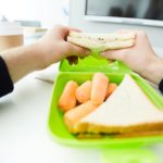 Hands of student holding vegetable sandwich over plastic container with fresh snack before eating it