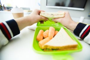 Hands of student holding vegetable sandwich over plastic container with fresh snack before eating it