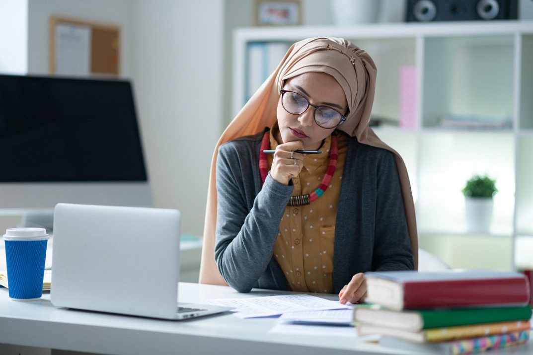 Teacher holding pen. Stylish Muslim teacher wearing glasses holding pen correcting tests