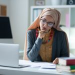 Teacher holding pen. Stylish Muslim teacher wearing glasses holding pen correcting tests