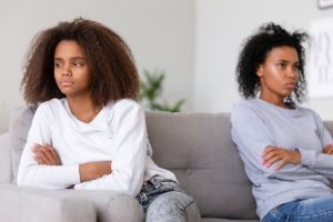 Stubborn african american teen daughter ignoring angry annoyed mom avoiding not talking after conflict, upset teenage girl and sad mother sitting on sofa with arms crossed, black family fight concept