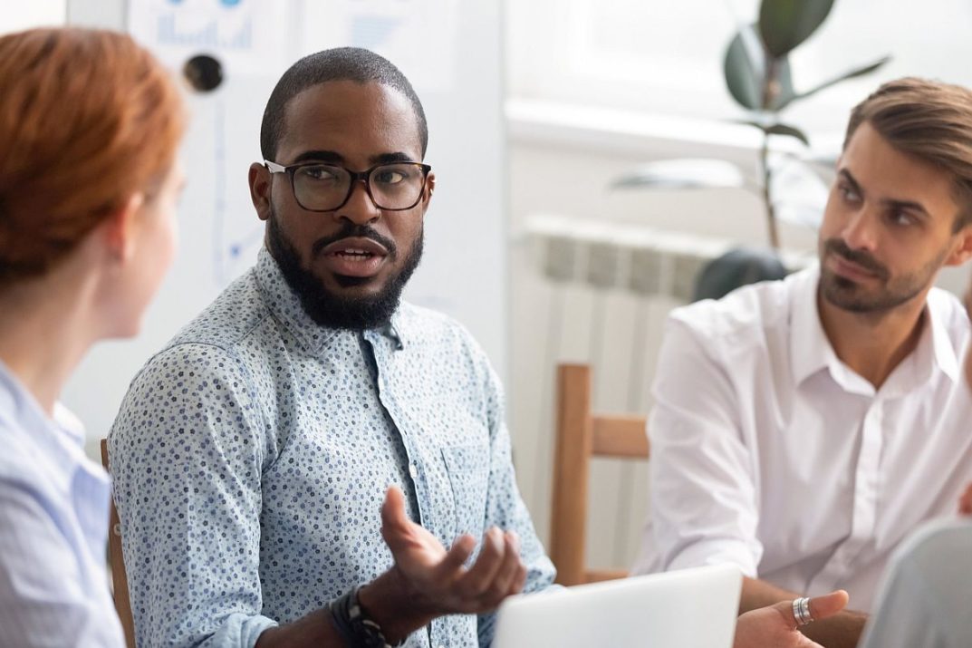 Serious confident african american black business coach leader mentor explaining caucasian colleagues clients interns team new corporate strategy talking at office meeting seminar workshop training.