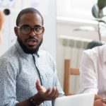 Serious confident african american black business coach leader mentor explaining caucasian colleagues clients interns team new corporate strategy talking at office meeting seminar workshop training.