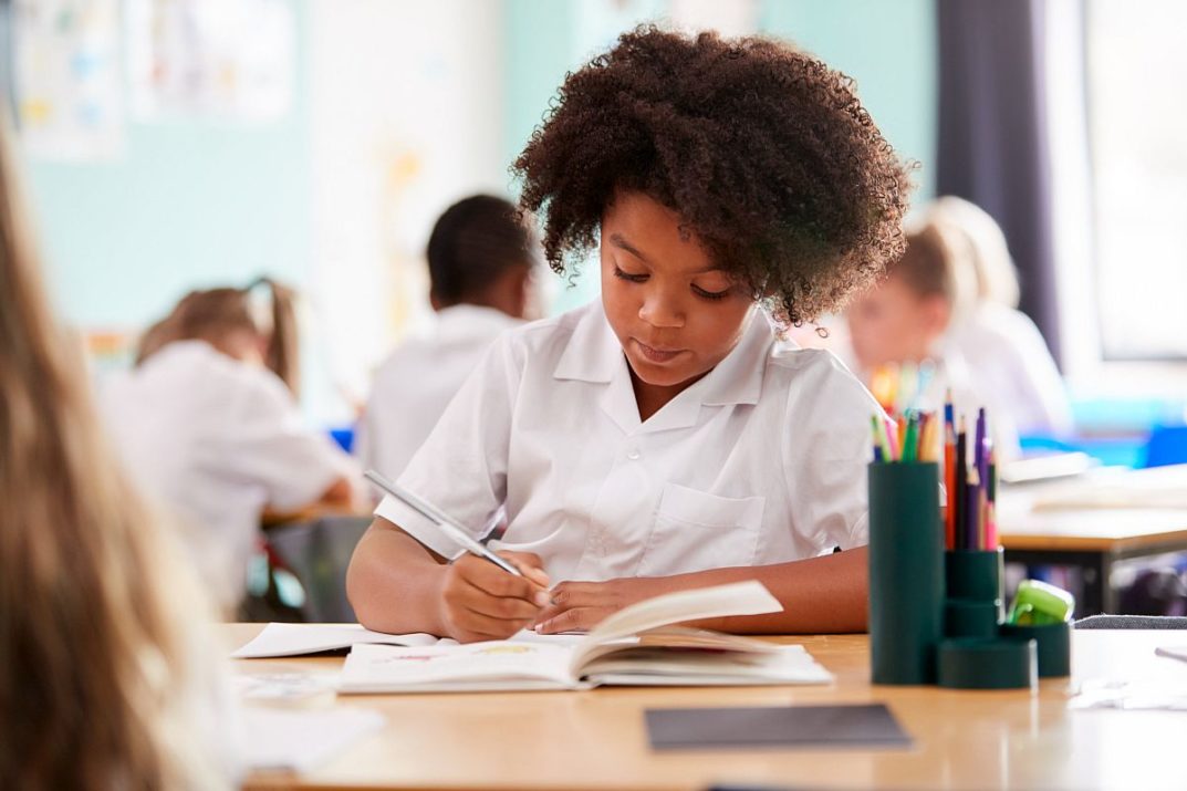 Elementary School Pupil Wearing Uniform Working At Desk; ; Essay Lesson Plan concept