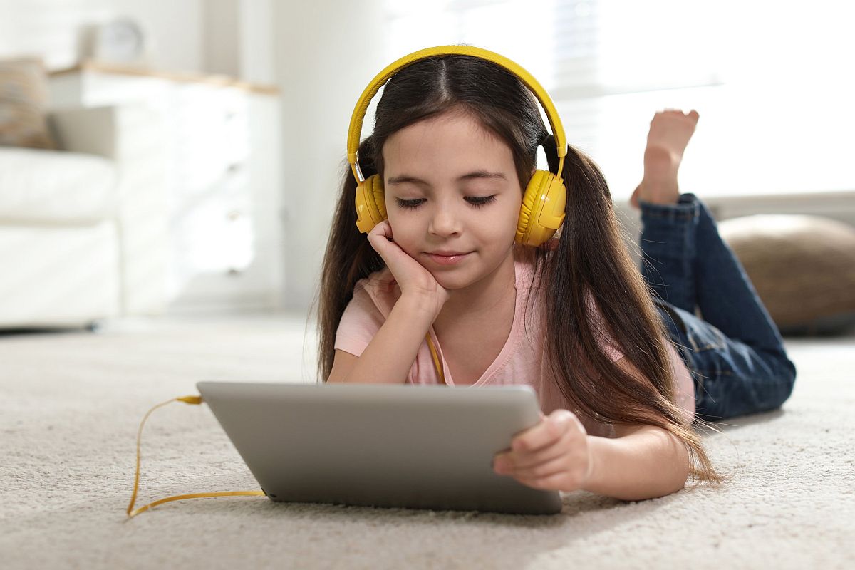 Cute little girl with headphones and tablet listening to audiobook at home; science podcasts for students concept