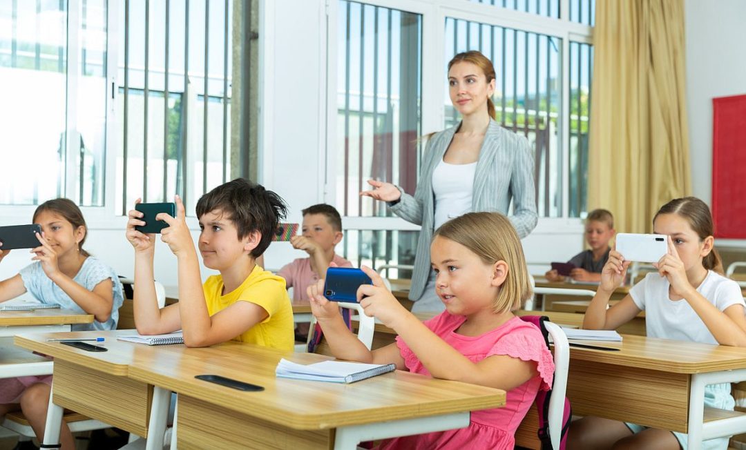 Schoolchildren with smartphones sitting in classroom