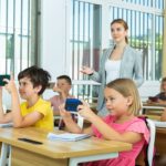 Schoolchildren with smartphones sitting in classroom