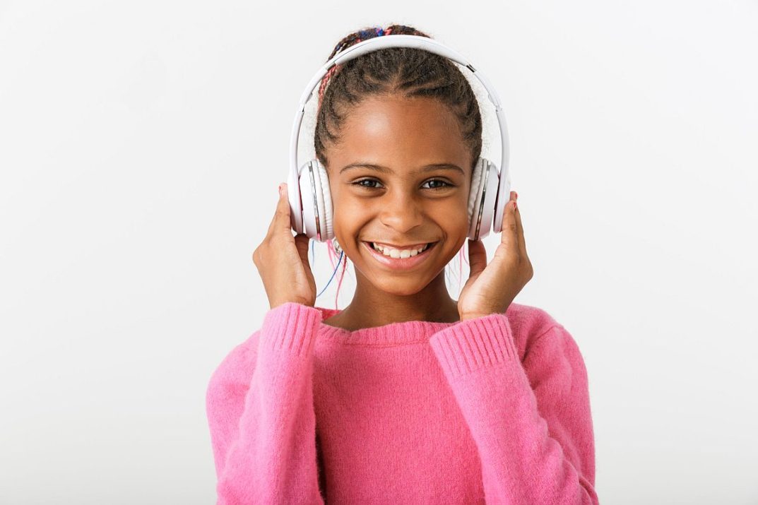 Image of pleased african american girl listening music with headphones while smiling isolated over white background