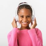 Image of pleased african american girl listening music with headphones while smiling isolated over white background