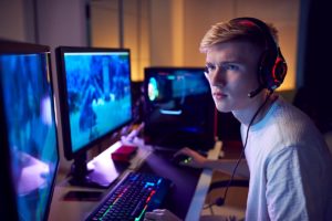 Teenage Boy Wearing Headset Gaming At Home Using Dual Computer Screens