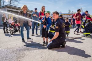 JARFALLA, SWEDEN - MAY 6, 2018: Side view of children and parents at a fire station trying a fire hose and sprays water, assisted by a fireman in Jarfalla May 6, 2018.
