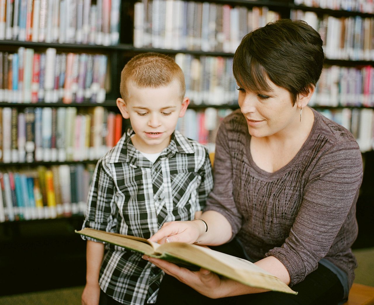 Paraeducator works with young student in library; paraeducators and teachers concept