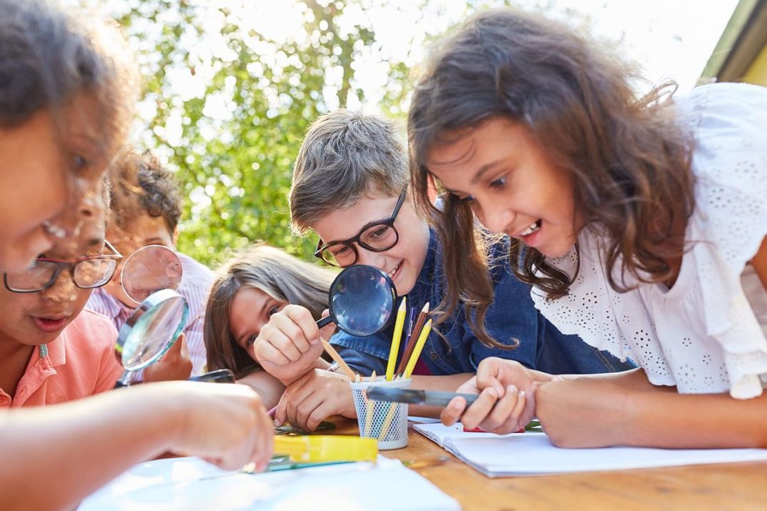 Several children in outdoor classroom using magnifying glasses; botany lessons concept