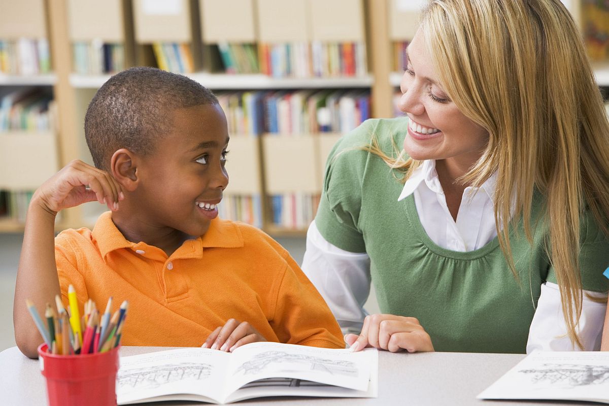 Young boy with book smiling at adult woman; welcome new students concept