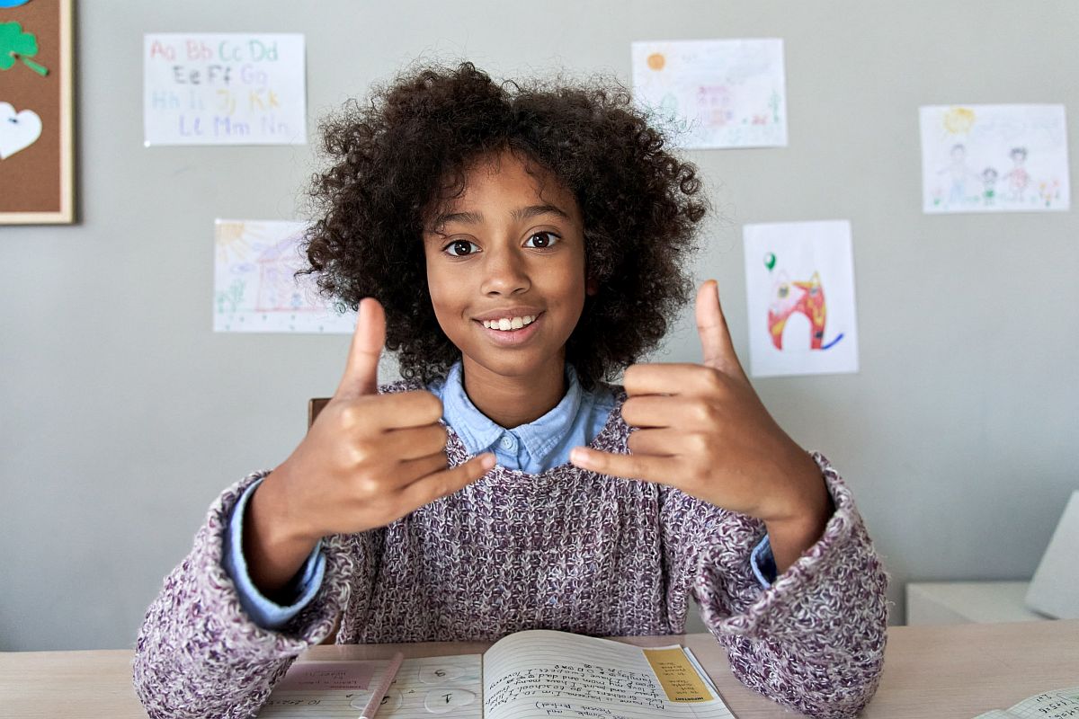 Smiling child at desk giving a thumbs up; individualized education program concept
