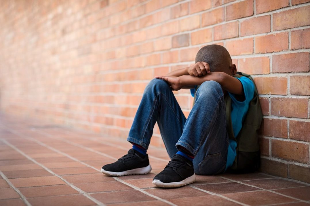 Young boy sitting on the floor alone with his head resting on his arms; social emotional concept