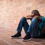 Young boy sitting on the floor alone with his head resting on his arms; social emotional concept