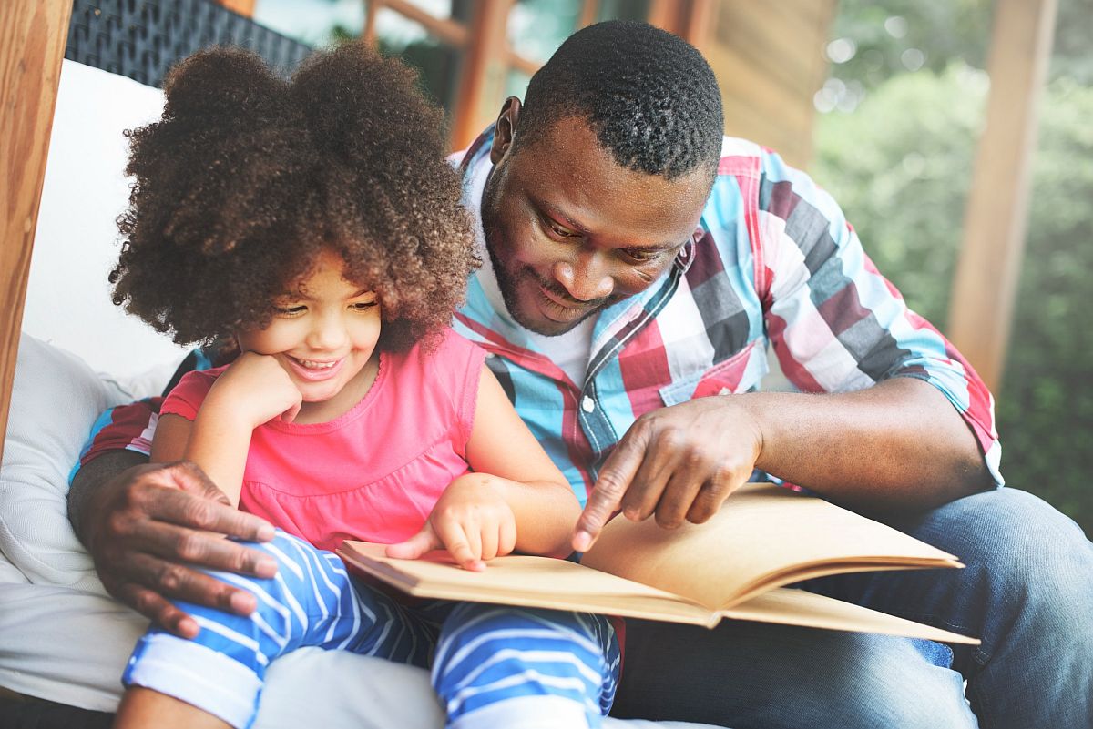 Adult man and young child sitting together, reading a book; learning disabilities concept