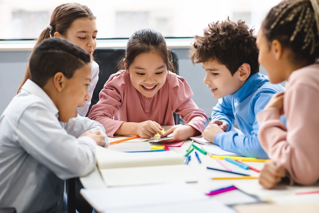 Happy children sitting at a table, looking at a phone; neurodiverse students concept