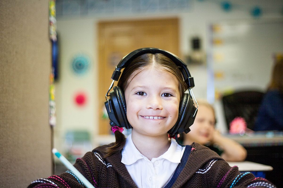 Child at desk in classroom wearing headphones; English Language Learners concept