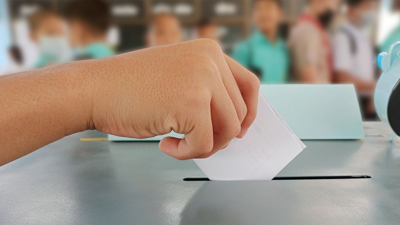 Close-up of hand inserting ballot into box; voting lesson plans concept
