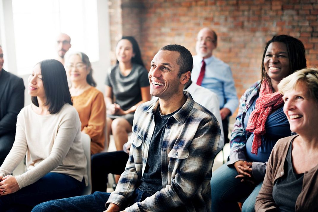 Group of laughing adults, seated and listening to speaker; professional development sessions concept