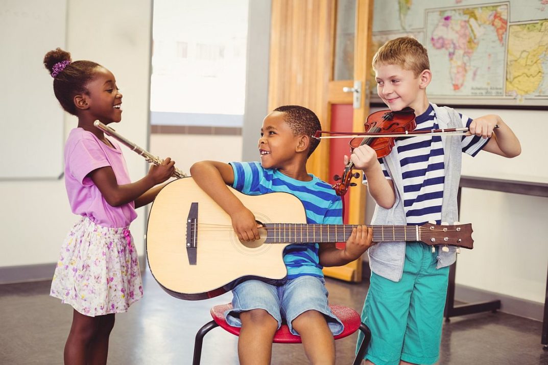 Three smiling children in a classroom, practicing different instruments; improve social emotional skills concept