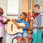Three smiling children in a classroom, practicing different instruments; improve social emotional skills concept
