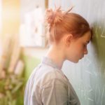 Student with her head against the blackboard, full of equations; academic self-esteem concept