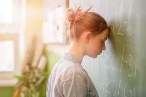 Student with her head against the blackboard, full of equations; academic self-esteem concept