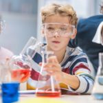 Young students mixing liquids in beakers, with teacher supervising; chemistry classroom concept