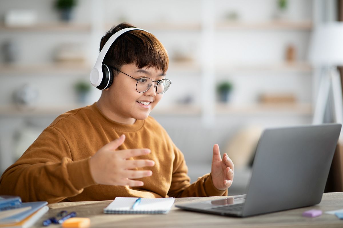 Smiling student wearing headphones, looking at laptop; virtual field trips concept