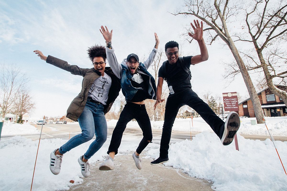 Laughing teens jumping on snowy sidewalk; add physical activity concept.