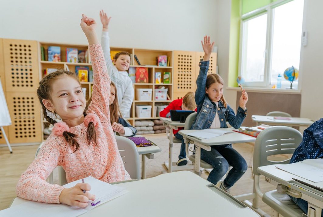 Children in classroom, raising their hands; nano-learning concept.