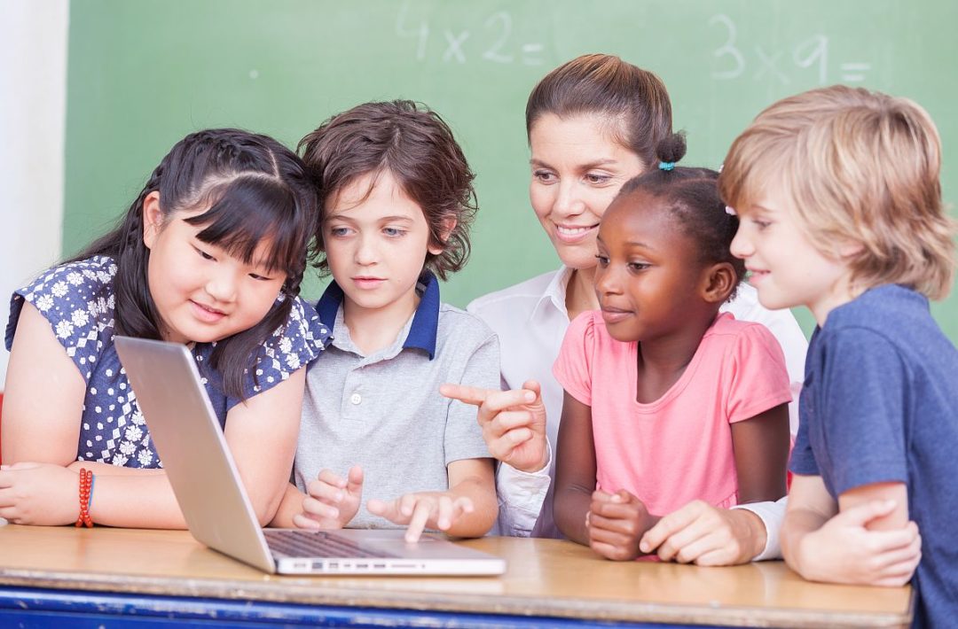 Elementary students and teacher looking at laptop; nano-learning classroom concept