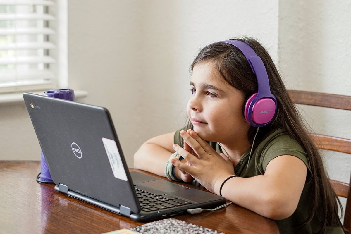 Child watching something on a laptop, wearing headphones; nano-learning concept.